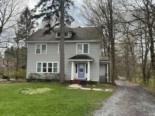 Gray and white Main House with a dark roof, central entry, mature trees, and gravel drive