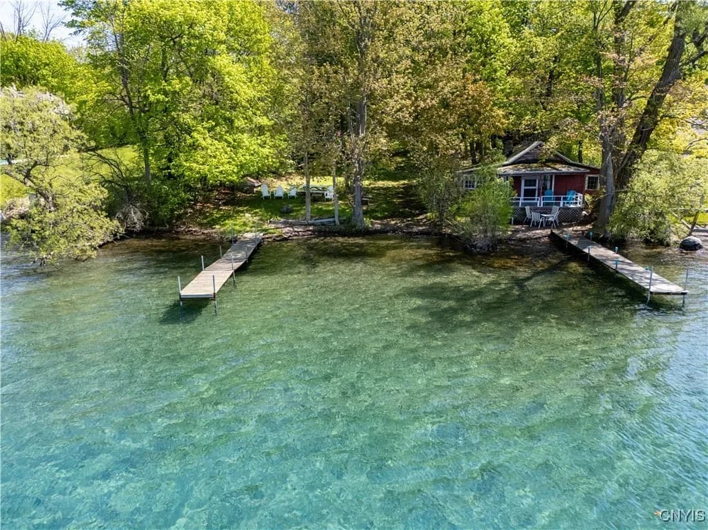 The wooded Landing shoreline, two docks, and red Lakefront Cottage seen from Skaneateles Lake